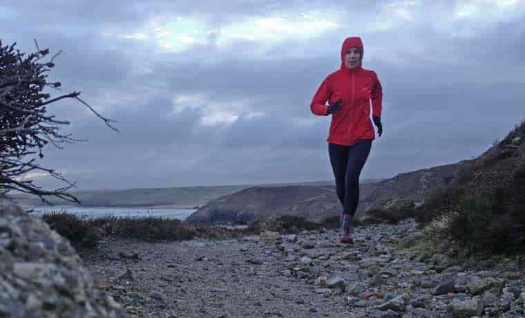 Woman with hood running on coast path