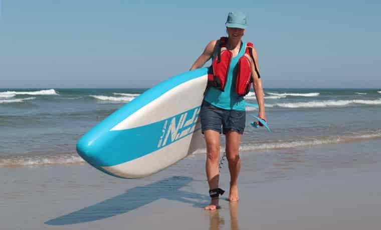 Soaked woman carrying SUP out of sea