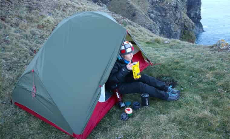 Woman eating backpacking food next to tent