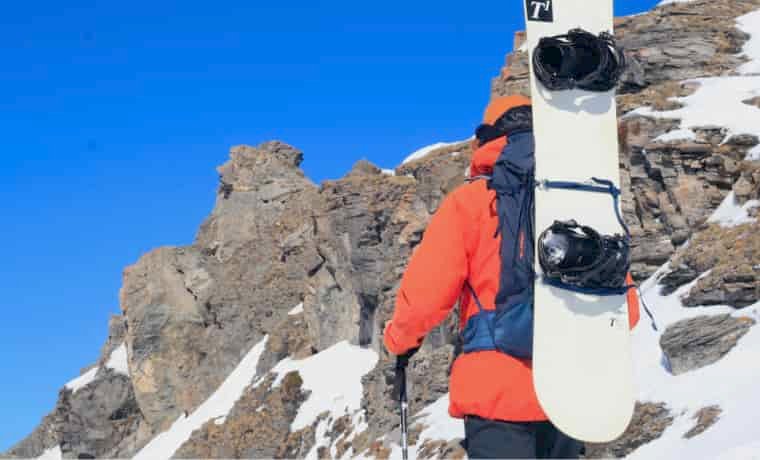 Snowboarder hiking with board on back