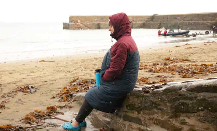 Woman sitting on beach in jacket