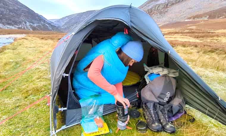 woman in sleeping bag making coffee in tent